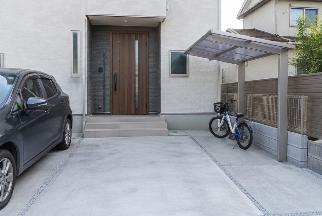 コンクリートの駐車場の横に屋根付きの自転車置き場がある住宅