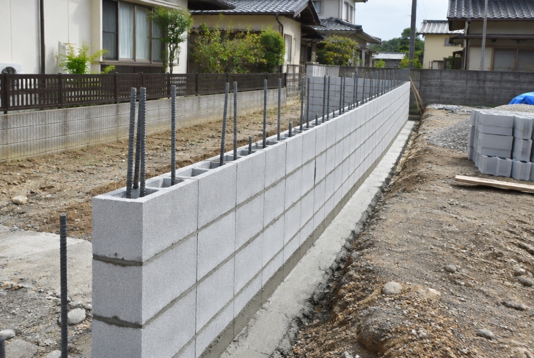 鉄筋を立てながらコンクリートブロックを積む境界の塀の工事