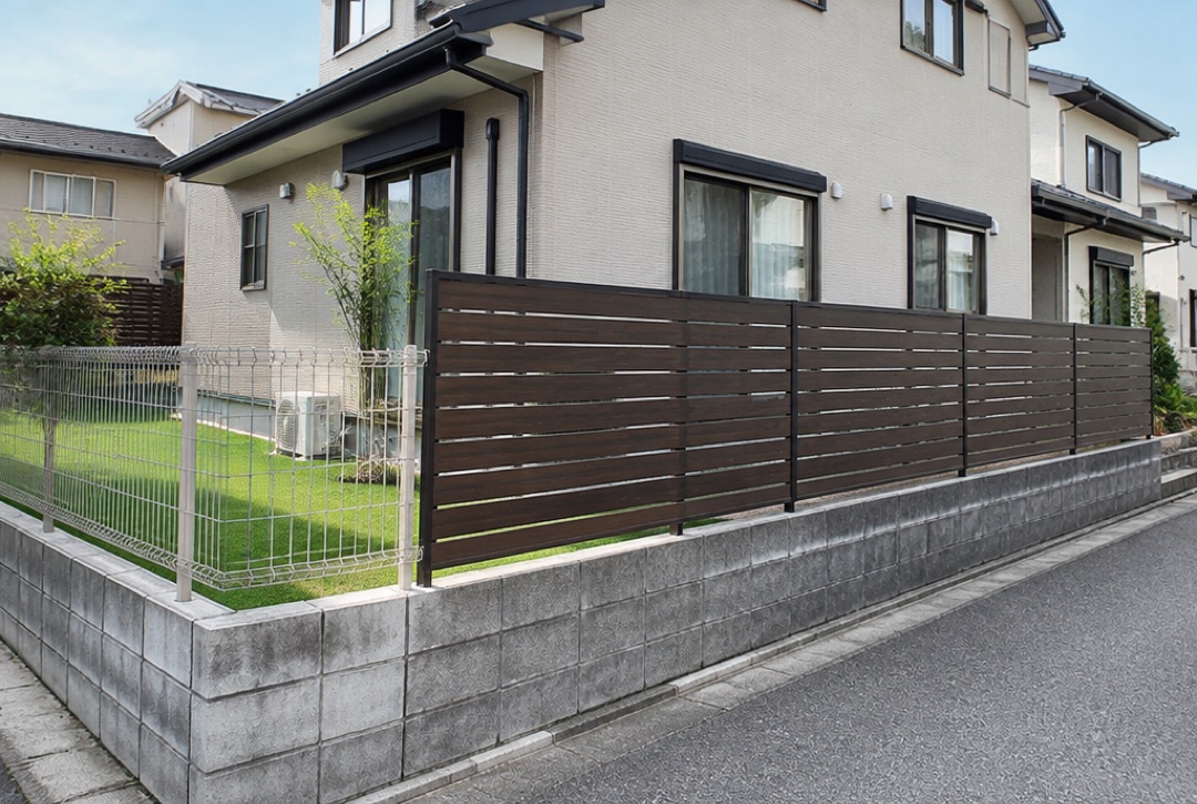 ブロックの上に目隠しフェンスを立て、別の面はメッシュフェンスにした住宅